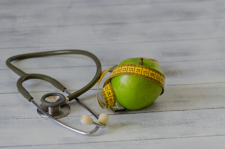 Green apple with measuring tape, stethoscope on white wooden background.Dieting concept.の写真素材