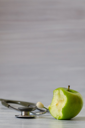 Fresh green apple with a bite isolated and stethoscope  on white  wooden backgroundの写真素材