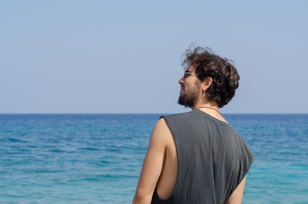 Bearded young man who wears earring is smiling in front of the sea while looking his left and looking forward.の写真素材