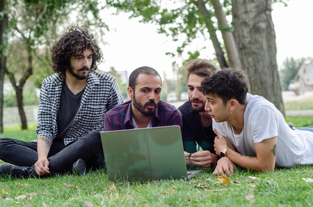 Four young men lie on the grass and work on the laptop computer.の写真素材