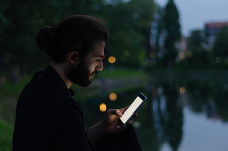The young man is shopping on the mobile telephone  when at the sunset.の写真素材
