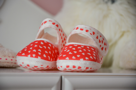 Red-white baby booties are  on the chest of drawer.の写真素材