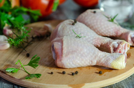 Raw chicken legs with  tomatoes,onion on a circular wooden board on white background.Close upの写真素材