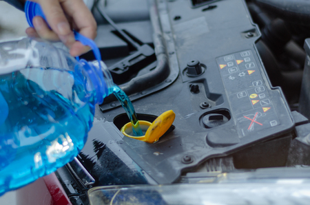 Male is holding  bottle of blue antifreeze in hands and pouring antifreeze liquid for washing car screen.の写真素材