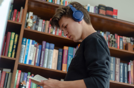 The teenage listens to music and reads book in front of library at homeの写真素材