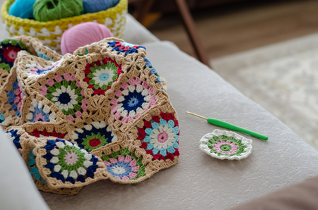 Multicolored plaid squares of crocheted on a cream colored seat background. In a basket with  of yarn, colors are green, pink, blue and  turquoiseの写真素材