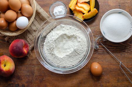 The cake ingredients and peach pie making on wooden table.
