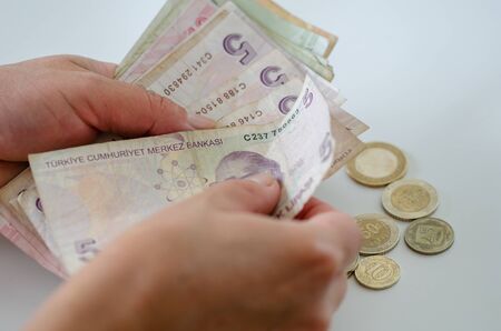 The woman is counting turkish banknote and coin on white background.