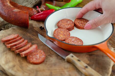 Turkish sausage sucuk slices  on a cutting board,close up.Woman is putting sausage sucuk slices on...