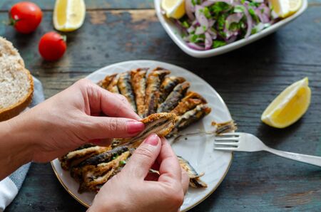 Fried anchovies fish and salad on wooden table.The woman is eating fish.の写真素材