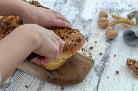 The woman is cutting the fresh bread in the kitchen, top view.