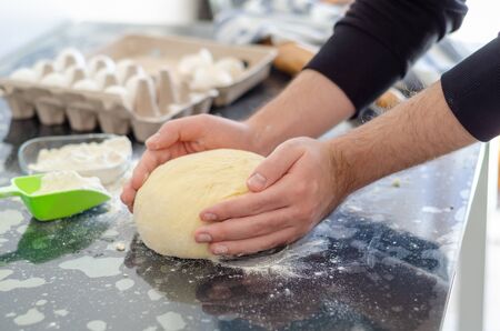 The young man is kneading dough on the table.
