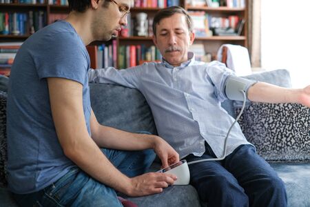 The young man measures his father's blood pressure at home.