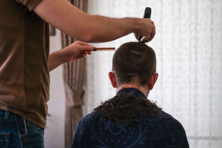 The young man is cutting father's hair with hair clipper during coronavirus quarantine isolation at...