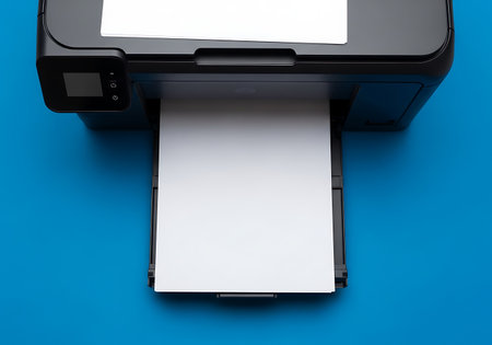 A black printer is shown from a top-down perspective against a bright blue background. White paper is visible in the input tray at the top and emerging from the output tray at the bottom. The printer has a small control panel with a screen and buttons on the left side.の素材