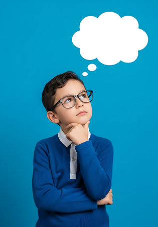 A young boy with glasses is shown thinking with a white cloud-shaped thought bubble above his head. He has his hand on his chin and is looking up against a solid blue background.の素材