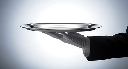 A silver tray is held by a hand wearing a white glove. The hand is attached to a black suit. The background is a gradient of gray to white.の素材