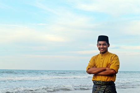 Guy in traditional dress of Malay beside the local beach covered with breathtaking blue sky.の素材