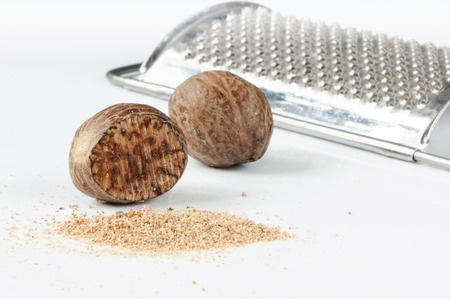 A closeup of nutmegs and a grater on the white background.