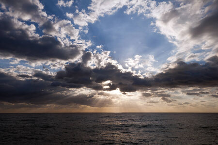 The sun shining through clouds over the seaの写真素材