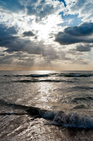 The sun shining through clouds over the seaの写真素材