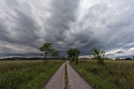 Summer landscape with a dirt road and the dark cloudy skyの写真素材