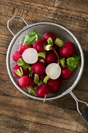 Several washed red radishes in a sieve on a wooden boardの写真素材