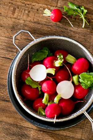 Several washed red radishes in a sieve on a wooden boardの写真素材