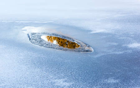 Ice around a small pool with water in which you see the reflection of the forestの写真素材