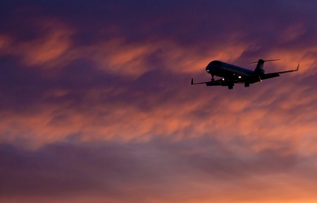 Airplane landing with vibrant sunset in backgroundの写真素材