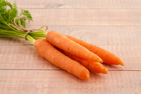 Fresh organic carrots with tops on wooden backgroundの写真素材
