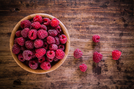 bright fresh organic raspberries in a bowl on old wooden backgroundの写真素材