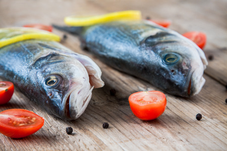 Two raw seabass fish with cherry tomatoes on a rustic wooden background
