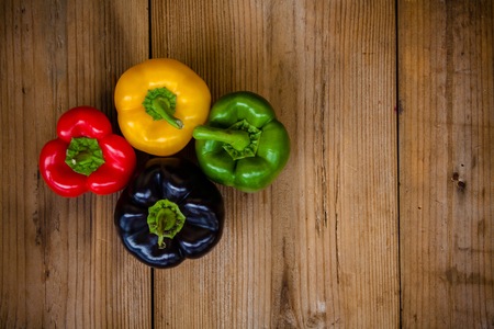 Red, green, black and yellow bell peppers on wooden backgroundの写真素材