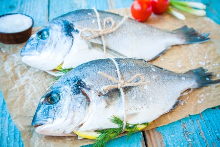 two raw dorada fishes with lemon, green onions and cherry tomatoes on a rustic backgroundの写真素材
