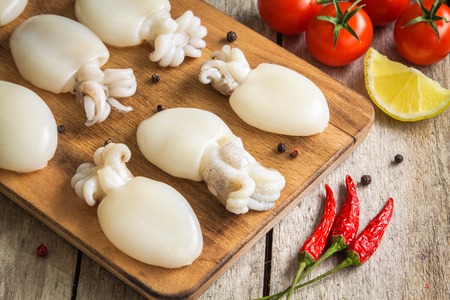 Raw babies cuttlefish  on a cutting board with tomatoes, chili peppers and lemon