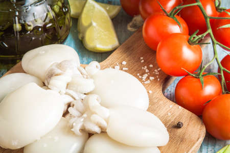 Raw babies cuttlefish  on a cutting board with tomatoes and lemon closeup