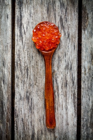 fresh red caviar in a wooden spoon on a rustic wooden backgroundの写真素材