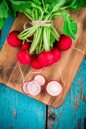 bundle of  bright fresh organic radishes with slices and green onion on wooden cutting board