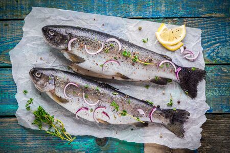 two raw trouts on paper with thyme and lemon and red onion slices on a rustic wooden table