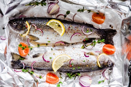two raw river trouts with thyme, lemon, red onion and tomatoes in foil for baking closeup