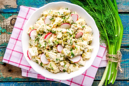 potato salad with fresh radishes in a white bowl  with dill and green onion on a rustic wooden tableの写真素材