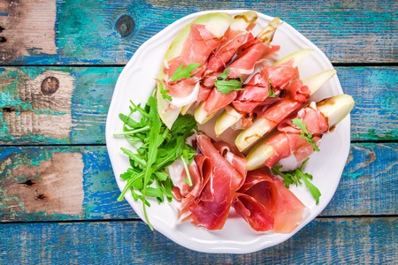 salad of fresh melon with thin slices of prosciutto, arugula leaves and balsamic sauce top viewの写真素材