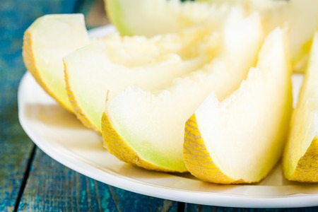 slices of fresh melon on a plate closeup on a rustic blue tableの写真素材
