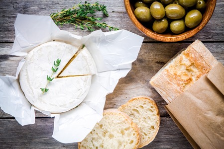 Whole Camembert cheese with thyme, olives and baguette on rustic tableの写真素材