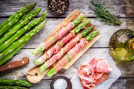Fresh organic asparagus wrapped in Parma ham on a cutting board top viewの写真素材