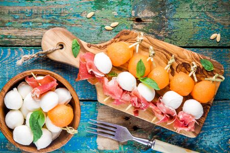 mozzarella and prosciutto with melon canapes with basil on rustic tableの写真素材