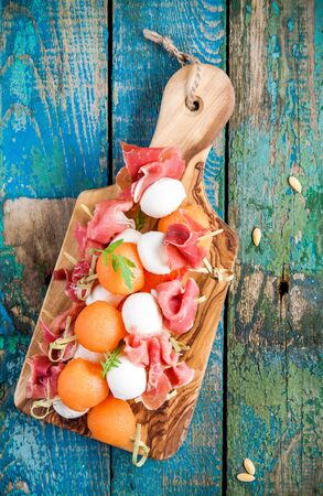 mozzarella and prosciutto with melon canapes on a cutting board on rustic tableの写真素材