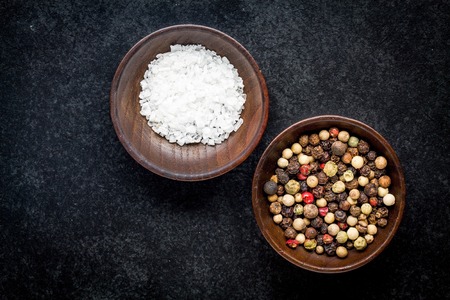 peppercorns and sea salt in a wooden bowl on a dark backgroundの写真素材
