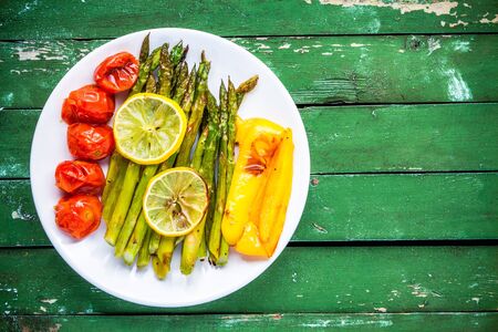 baked vegetables: asparagus, cherry tomatoespaprika, lemon in a plate on wooden tableの写真素材